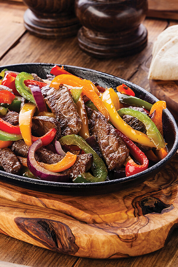 Beef strips and vegetables in frying pan on table